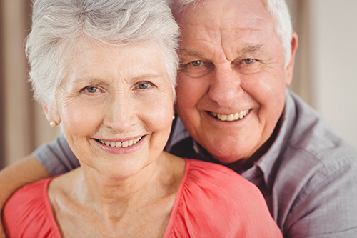 Elderly couple smiling at the camera embracing each other