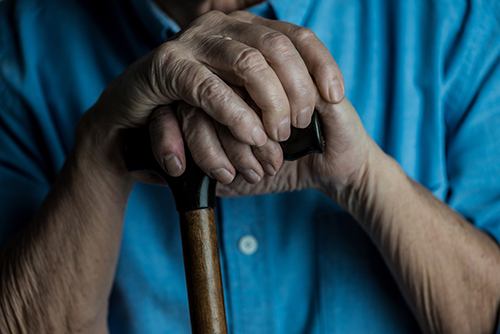 Dim lighting close up of elderly hands resting atop a walking cane